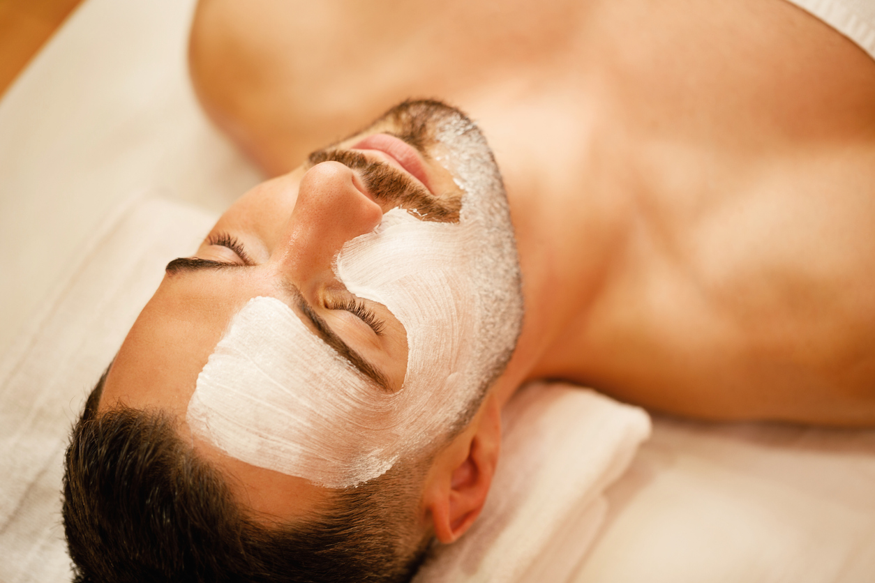 Close-up of man with white facial mask relaxing during treatment at beauty spa.
